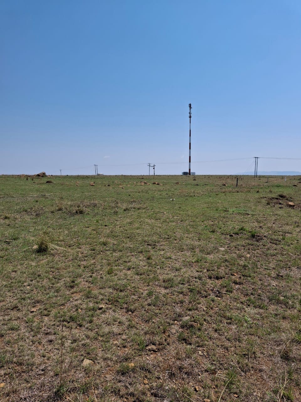 Open New Hope land under a clear sky, with the communications mast and power lines on the horizon